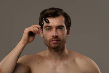 Bir adam alnında siyah yeşim bir silindir kullanıyor. Cilt bakımının bir parçası olarak yüz gençleştirme için..