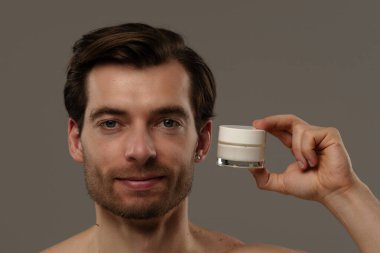 Bir adam cilt kremi kavanozuna odaklanmış bir ifadeyle bakar, muhtemelen cildine yararını göz önünde bulundurarak..