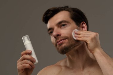 Yumuşak ışıklandırma altında cilt ürünü kullanan bir adam günlük bakım rutininde yüz bakımının önemini vurguluyor..