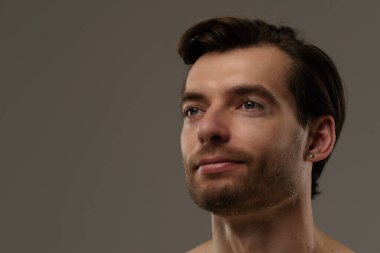 Düşünceli bir ifade sergileyen bir adamın portresi. Kısa saçları ve bir küpesi var. Benzersiz tarzının altını çiziyor..