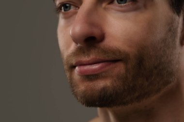 Düşünceli bir ifade sergileyen bir adamın yakın plan portresi. Kısa saçları ve bir küpesi var. Benzersiz tarzının altını çiziyor..