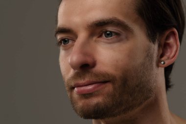 Düşünceli bir ifade sergileyen bir adamın portresi. Kısa saçları ve bir küpesi var. Benzersiz tarzının altını çiziyor..