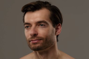 Düşünceli bir ifade sergileyen bir adamın portresi. Kısa saçları ve bir küpesi var. Benzersiz tarzının altını çiziyor..