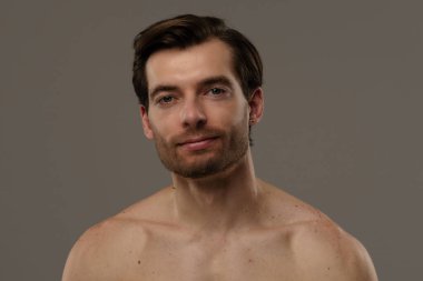 Düşünceli bir ifade sergileyen bir adamın portresi. Kısa saçları ve bir küpesi var. Benzersiz tarzının altını çiziyor..