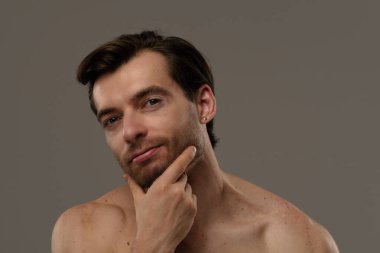 Düşünceli bir ifade sergileyen bir adamın portresi. Kısa saçları ve bir küpesi var. Benzersiz tarzının altını çiziyor..