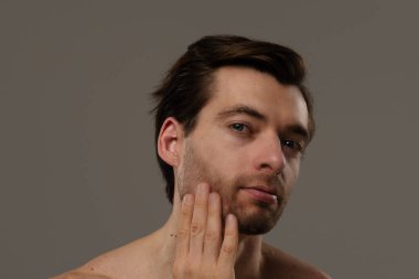 Düşünceli bir ifade sergileyen bir adamın portresi. Kısa saçları ve bir küpesi var. Benzersiz tarzının altını çiziyor..