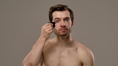 Kaslı bir adam yüz masajı için gua sha aracı kullanır, cilt bakımı, rahatlama ve gençleştirme teknikleri gösterir. Yavaş çekim