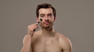 Bir adam alnında siyah yeşim taşıyla cilt yenileme rutininin bir parçası olarak duruyor. Yavaş çekim