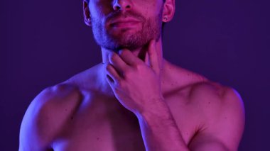 Bir erkek gövdesi mavi ve mor ışığın sanatsal bir karışımında vurgulanır ve dramatik bir görsel etki yaratır. Yavaş çekim