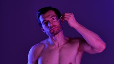 Bir adam deri dokusunu geliştirmek ve beslenmek için deri serumunu nazikçe kullanır. Yavaş çekim