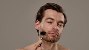 Bir adam alnında siyah yeşim taşıyla cilt yenileme rutininin bir parçası olarak duruyor. Yavaş çekim