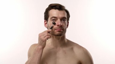 Bir adam alnında siyah yeşim taşıyla cilt yenileme rutininin bir parçası olarak duruyor. Yavaş çekim