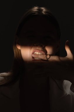 Bir kadının gölgeli portresi parmağından ısırıyor, yüzükle süslenip gizemli bir görüntü oluşturuyor..