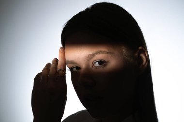 Bir kadının yüzünü gösteren çarpıcı bir portre. Işık huzmesi ve gölgeyle bölünmüş, dramatik ve gizemli bir etki yaratıyor..