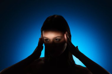 Yüzünde gölgeler olan bir kadının dingin portresi, canlı mavi bir arkaplan üzerine kurulmuş..