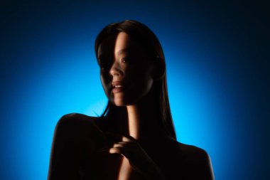 Yüzünde gölgeler olan bir kadının dingin portresi, canlı mavi bir arkaplan üzerine kurulmuş..