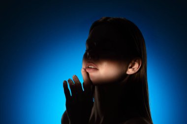 Yüzünde gölgeler olan bir kadının dingin portresi, canlı mavi bir arkaplan üzerine kurulmuş..