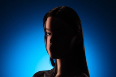 Yüzünde gölgeler olan bir kadının dingin portresi, canlı mavi bir arkaplan üzerine kurulmuş..