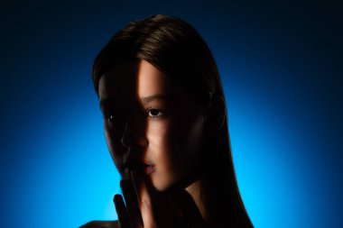 Yüzünde gölgeler olan bir kadının dingin portresi, canlı mavi bir arkaplan üzerine kurulmuş..