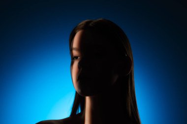 Yüzünde gölgeler olan bir kadının dingin portresi, canlı mavi bir arkaplan üzerine kurulmuş..