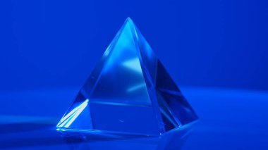 Canlı mavi ışığı yansıtan cam bir piramit nesnesi eşleşen bir arka plana karşı büyüleyici bir görsel etki yaratır. Makro