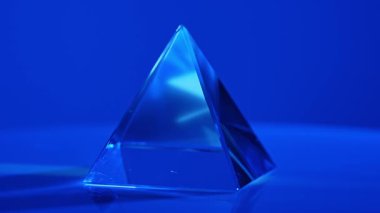 Canlı mavi ışığı yansıtan cam bir piramit nesnesi eşleşen bir arka plana karşı büyüleyici bir görsel etki yaratır. Macro, ağır çekim.
