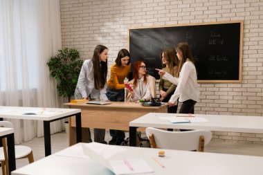 Bir grup öğrenci öğretmenlerin etrafında toplanıyor. Sınıfa telefon edip aktif olarak bir proje üzerinde çalışıyorlar..