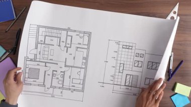 Bir grup profesyonel, ahşap bir masada mimari bir yapı planı üzerinde işbirliği içinde çalışıyor. Üst çekim, yavaş çekim.