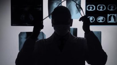 Tıbbi ortamdaki bir doktor röntgen görüntülerini inceliyor. Silüet, tıbbi sürece vurgu yapıyor. Yavaş çekim