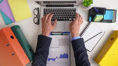 Bir iş adamı, ofis malzemeleriyle çevrili finansal verileri analiz eden bir dizüstü bilgisayar üzerinde çalışıyor. Üst çekim