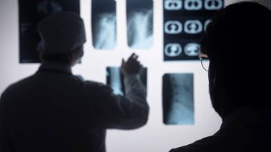 Tıbbi uzmanlar röntgen taramalarını inceleyip tartışıyor, gelişmiş görüntüleme teknolojisiyle tanı kavrayışlarını vurguluyorlar..