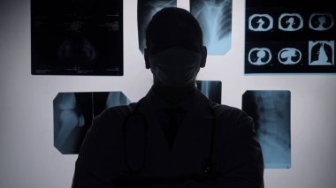 Tıbbi ortamdaki bir doktor röntgen görüntülerini inceliyor. Silüet, tıbbi sürece vurgu yapıyor..