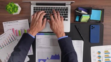Bir iş adamı, ofis malzemeleriyle çevrili finansal verileri analiz eden bir dizüstü bilgisayar üzerinde çalışıyor. Üst çekim