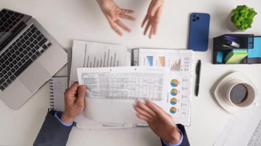 Grafikler, kağıtlar ve ellerle yapılan iş toplantısı tartışma ve strateji planlamasını vurguluyor. Üst çekim, yavaş çekim.