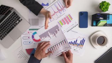 Bir iş toplantısında veri analizi ve strateji planlaması ele alındı. Takım üyeleri bilinçli kararlar almak için çizelgeleri ve grafikleri tartışırlar. Üst çekim