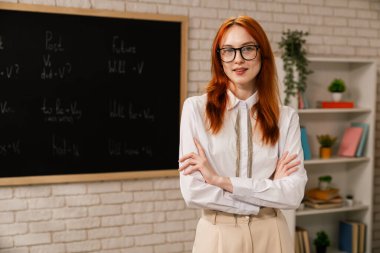 Bir öğretmen İngilizce fiil zamanlarını gösteren bir tahtanın yanında duruyor, şimdiki, geçmiş ve gelecek.