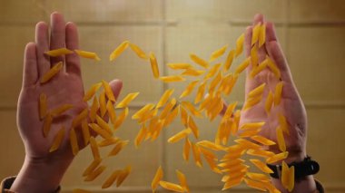 Penne makarnasının düşüşünü yakalamak için uzanan eller, düz kahverengi bir fonda yakalanır. Yavaş çekim