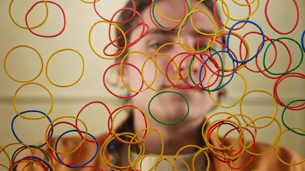Renkli lastik bantların canlı bir görüntüsü bulanık bir yüzün önüne asılır ve neşeli bir görsel efekt yaratır..