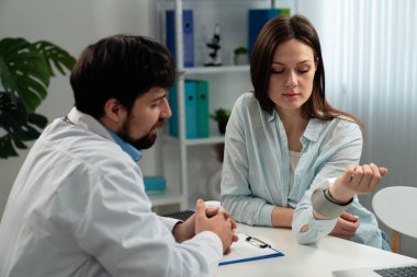 Bir doktor, modern bir muayenehanedeki bir hastaya dikkatle danışarak, sağlık sorunları ve tedavi seçeneklerini tartışır..