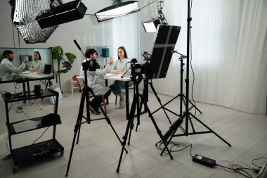 Sahne arkasında. Kameraların, ışıklandırma ekipmanlarının ve iki kişinin yer aldığı profesyonel bir video çekimi için modern bir kurgu..