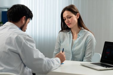 Bir kadın muayenehanede bir doktora danışıyor. Masadaki dizüstü bilgisayarla sağlıkla ilgili konuları tartışıyorlar..