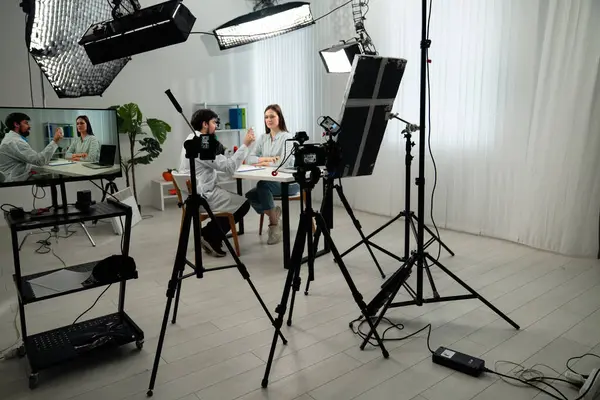 Sahne arkasında. Kameraların, ışıklandırma ekipmanlarının ve iki kişinin yer aldığı profesyonel bir video çekimi için modern bir kurgu..