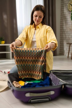 Bir kadın düşünceli bir şekilde giysilerini bavula koyup yolculuğa hazırlanıyor. Oda modern ve rahat..