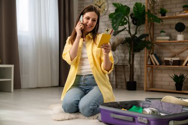 Bir kadın valizini toplar ve akıllı telefonuyla seyahate ya da tatile hazırlanırken konuşur..