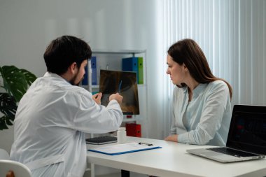Doktor, klinik ofis ortamındaki hastaya röntgen sonuçlarını açıklar. Odaklanmış ve meşgul görünüyorlar..