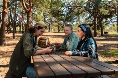 Güneşli bir park ortamında piknik masasında dinlenen üç arkadaş. Birbirine eşlik eden ve dışarıda eğlenen üç arkadaş..