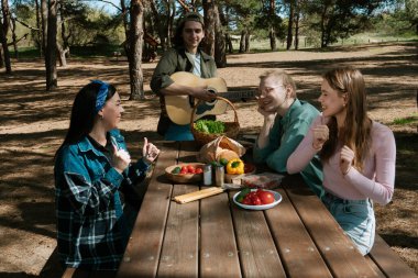 Bir grup arkadaş piknik için toplanır, güneşli bir açık hava ortamında yemek ve müziğin tadını çıkarırlar, rahatlamayı teşvik ederler..
