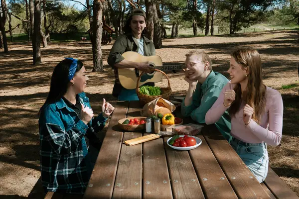 Bir grup arkadaş piknik için toplanır, güneşli bir açık hava ortamında yemek ve müziğin tadını çıkarırlar, rahatlamayı teşvik ederler..