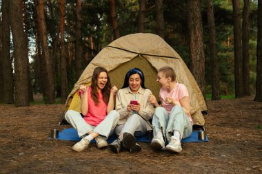 Bir grup arkadaş ormanda kamp yaparken eğlenceli bir anı paylaşıyor. Çadırın dışında oturmuş, doğanın tadını çıkarıyorlar..