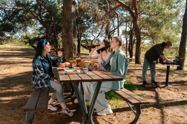 Bir grup arkadaş ormanda piknik yapıyor. Yiyecek ve içeceklerin tadını çıkarıyorlar..